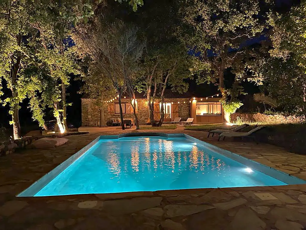 La piscine de Baraccò Argia éclairée la nuit, guirlandes lumineuses et façade de pierre de la bergerie